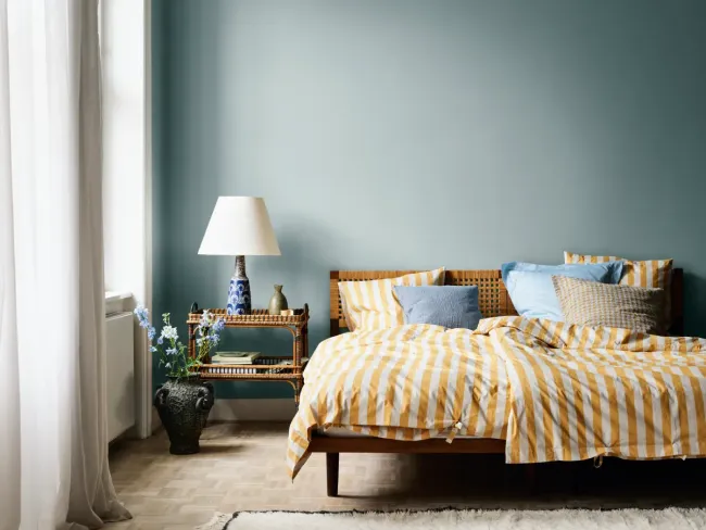 Un dormitorio con cama, mesita de noche, lámpara y paredes azules.