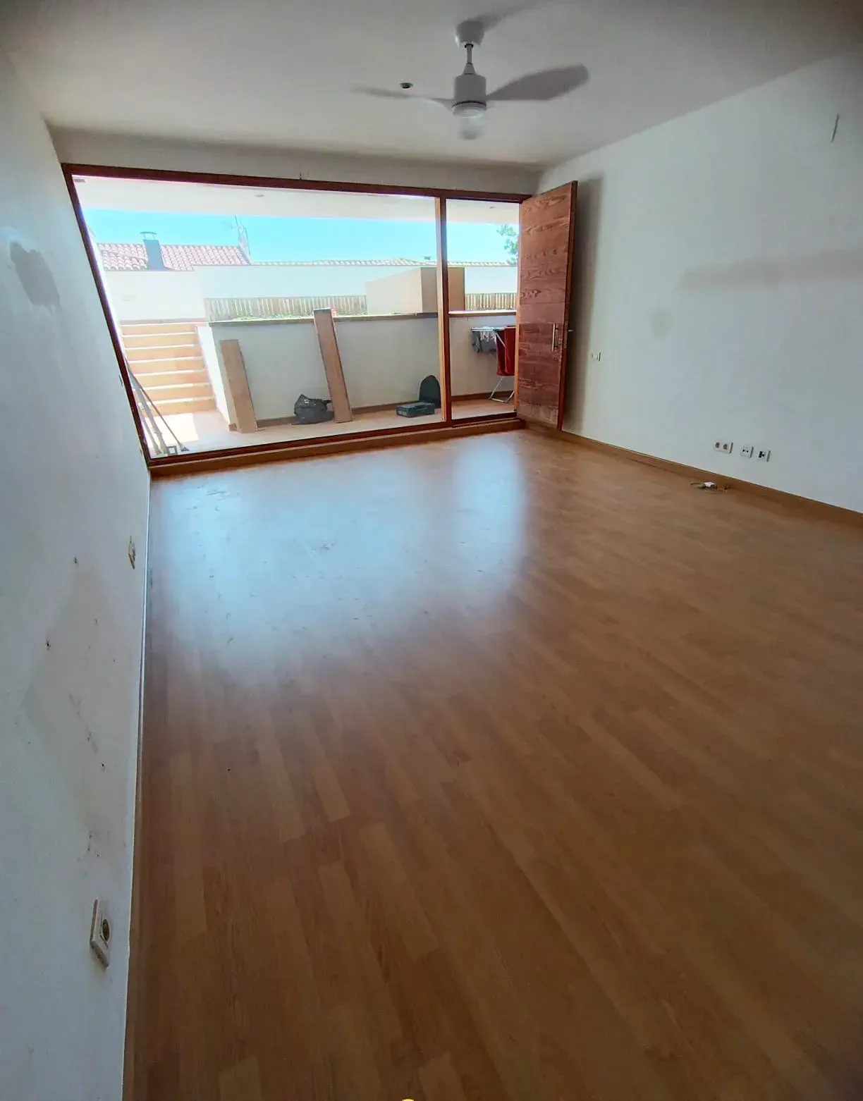 Una habitación vacía con pisos de madera y un ventilador de techo.