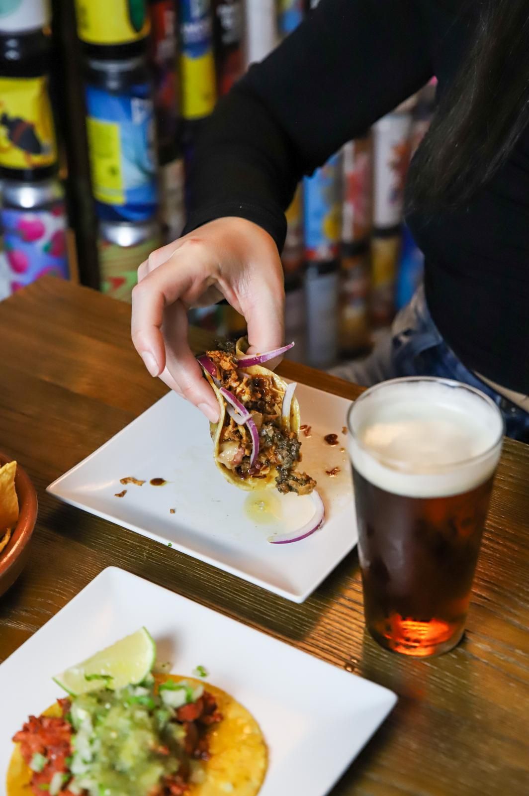 Una persona está poniendo un taco en un plato al lado de un vaso de cerveza.