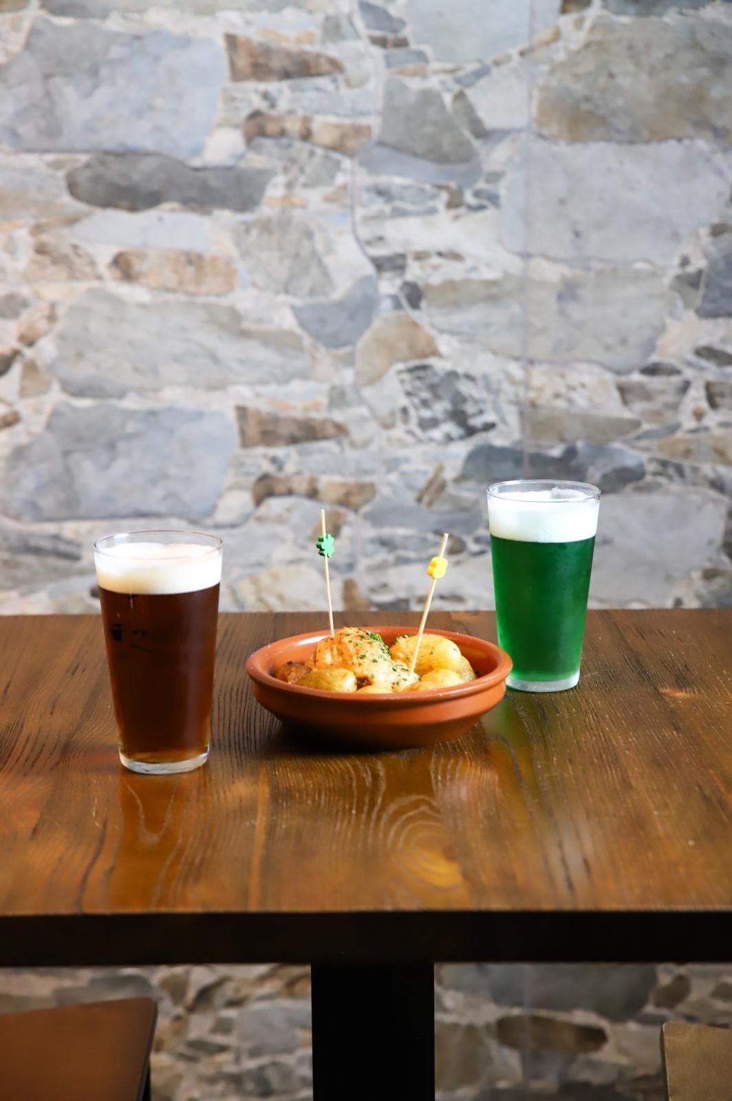 Sobre una mesa de madera hay dos vasos de cerveza y un bol de comida.