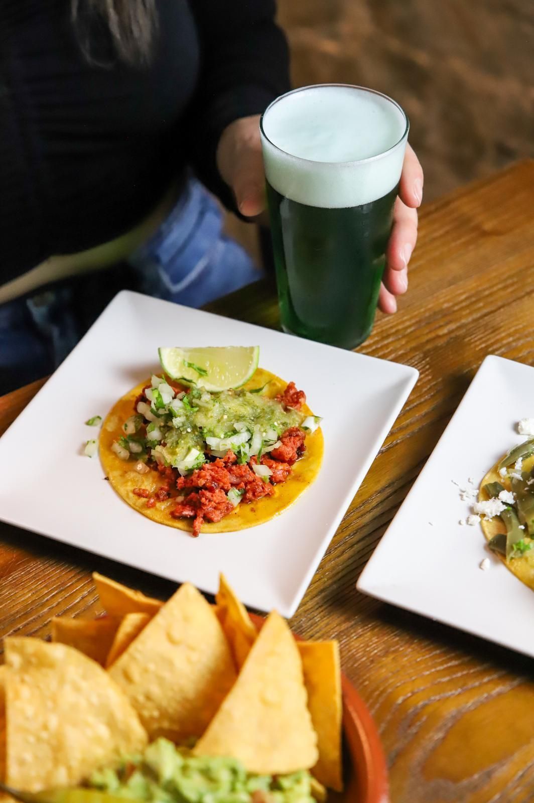 Una persona sostiene un vaso de cerveza al lado de un plato de comida.