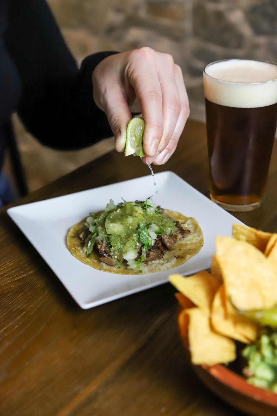 Una persona está exprimiendo un limón sobre un taco en un plato.