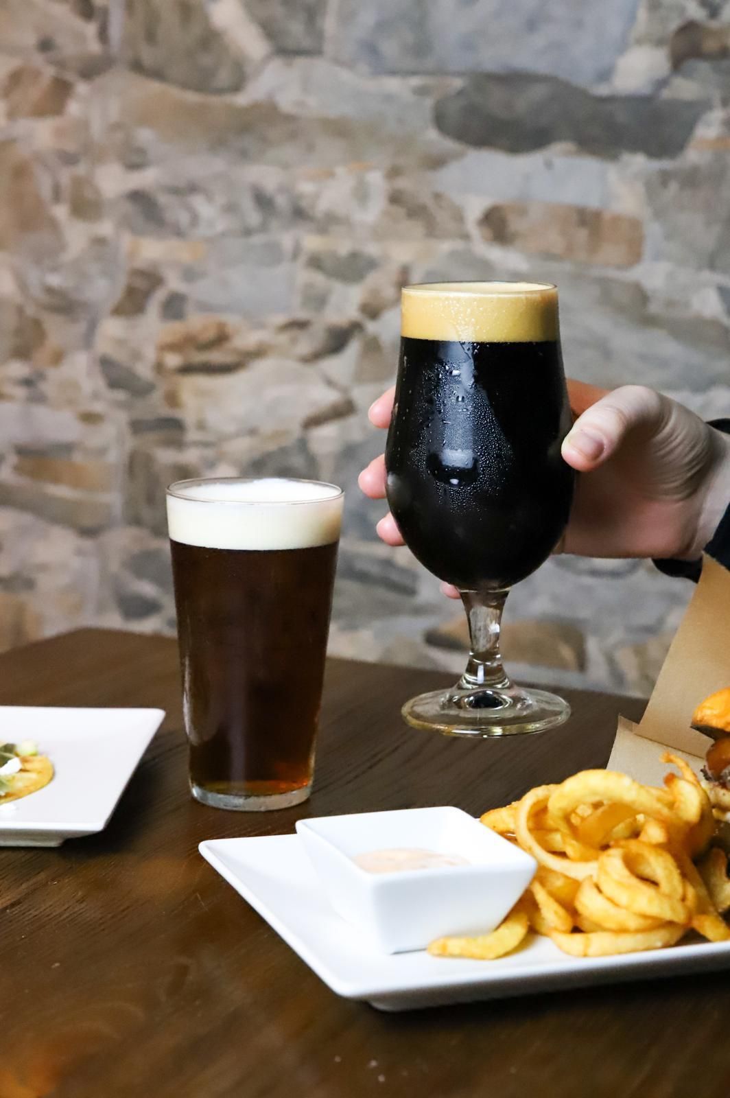 Una persona sostiene un vaso de cerveza al lado de un plato de papas fritas.