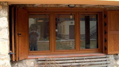 Un hombre está tomando una fotografía de una ventana con contraventanas de madera.