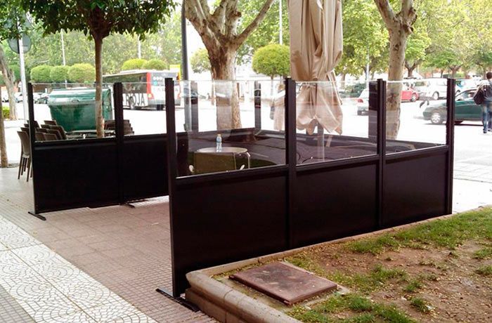 Un patio con mesas y sillas detrás de una barrera de vidrio.