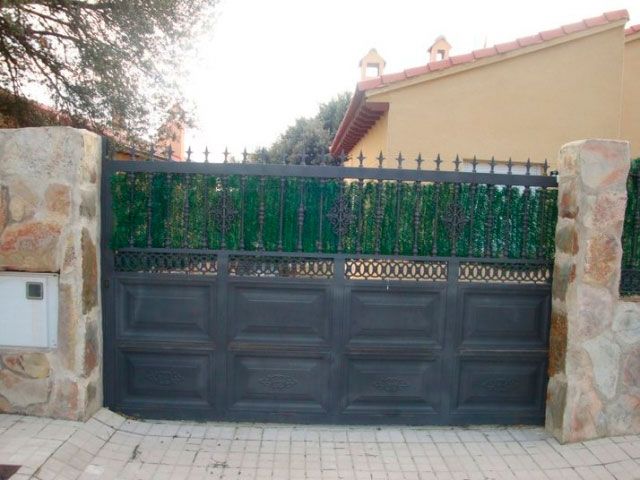 Una puerta negra con una valla verde detrás.
