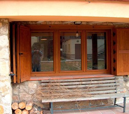Un banco de madera se encuentra frente a una ventana con contraventanas de madera.