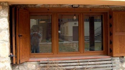 Un hombre está tomando una fotografía de una ventana con contraventanas de madera.