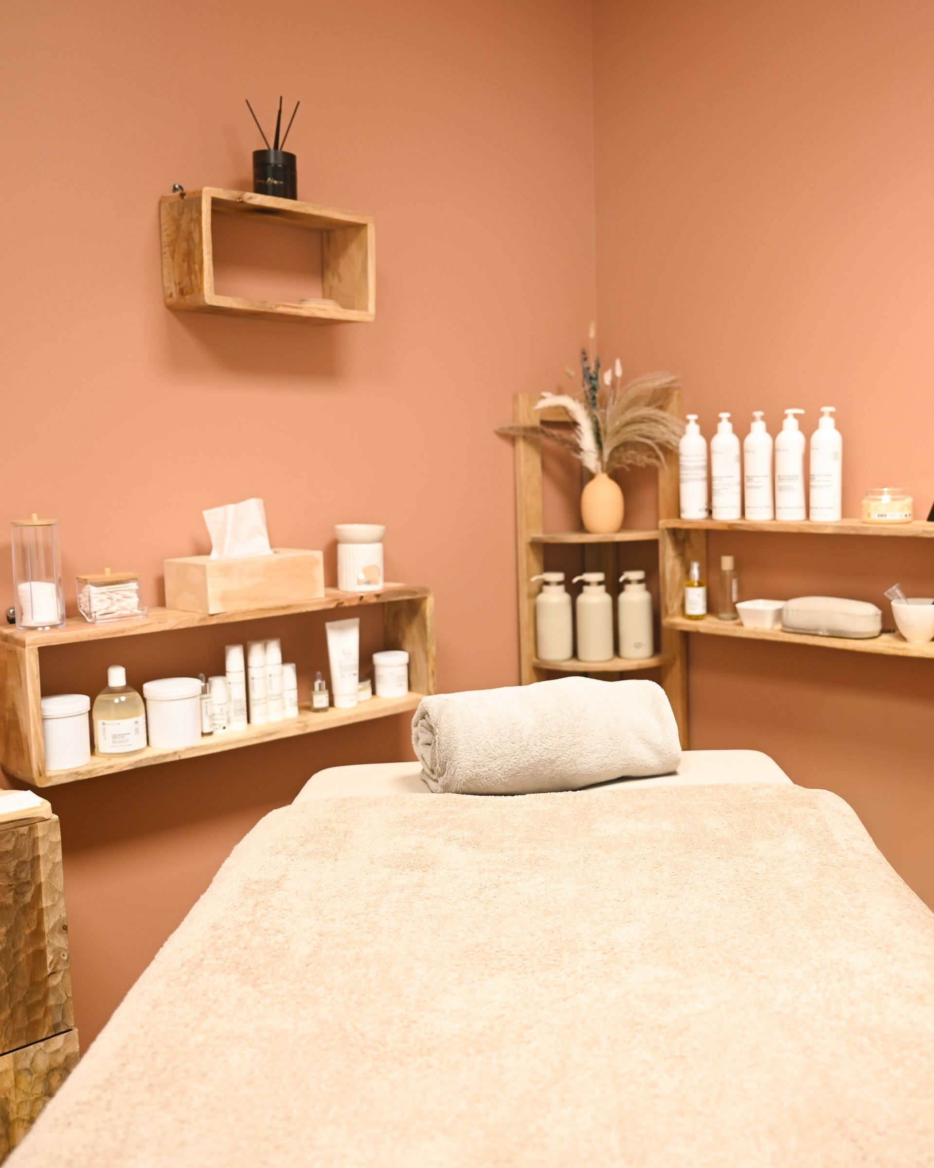 Cabine de soins de spa vide avec murs couleur pêche, table de massage et étagères de produits de soins de la peau