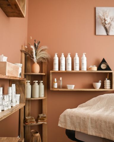 Salle de soins spa confortable avec murs en terre cuite, étagères de produits de soins de la peau et un lit au premier plan.