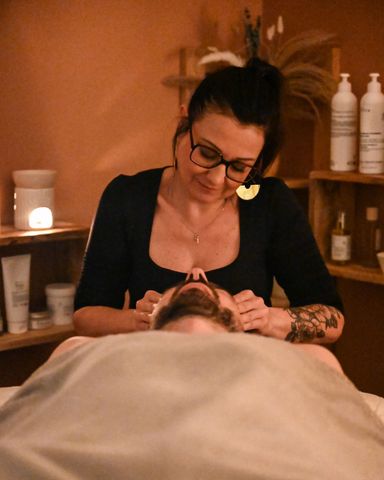 Une masseuse prodigue un soin du visage dans une salle de spa chauffée.