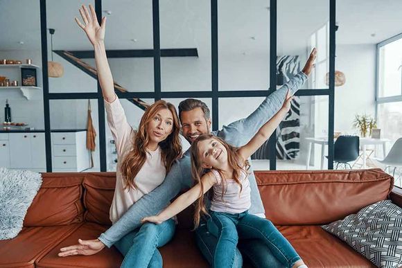 Eine Familie sitzt mit erhobenen Armen auf einem Sofa.