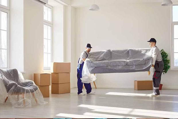 Zwei Männer tragen ein Sofa in einem Wohnzimmer.