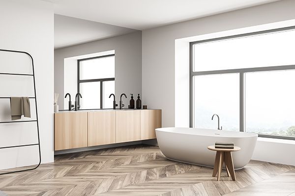 Une salle de bain neuve, avec un mur gris, et des meubles marron, un miroir et une baignoire.