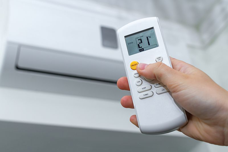 Une personne règle la température de son climatiseur avec une télécommande