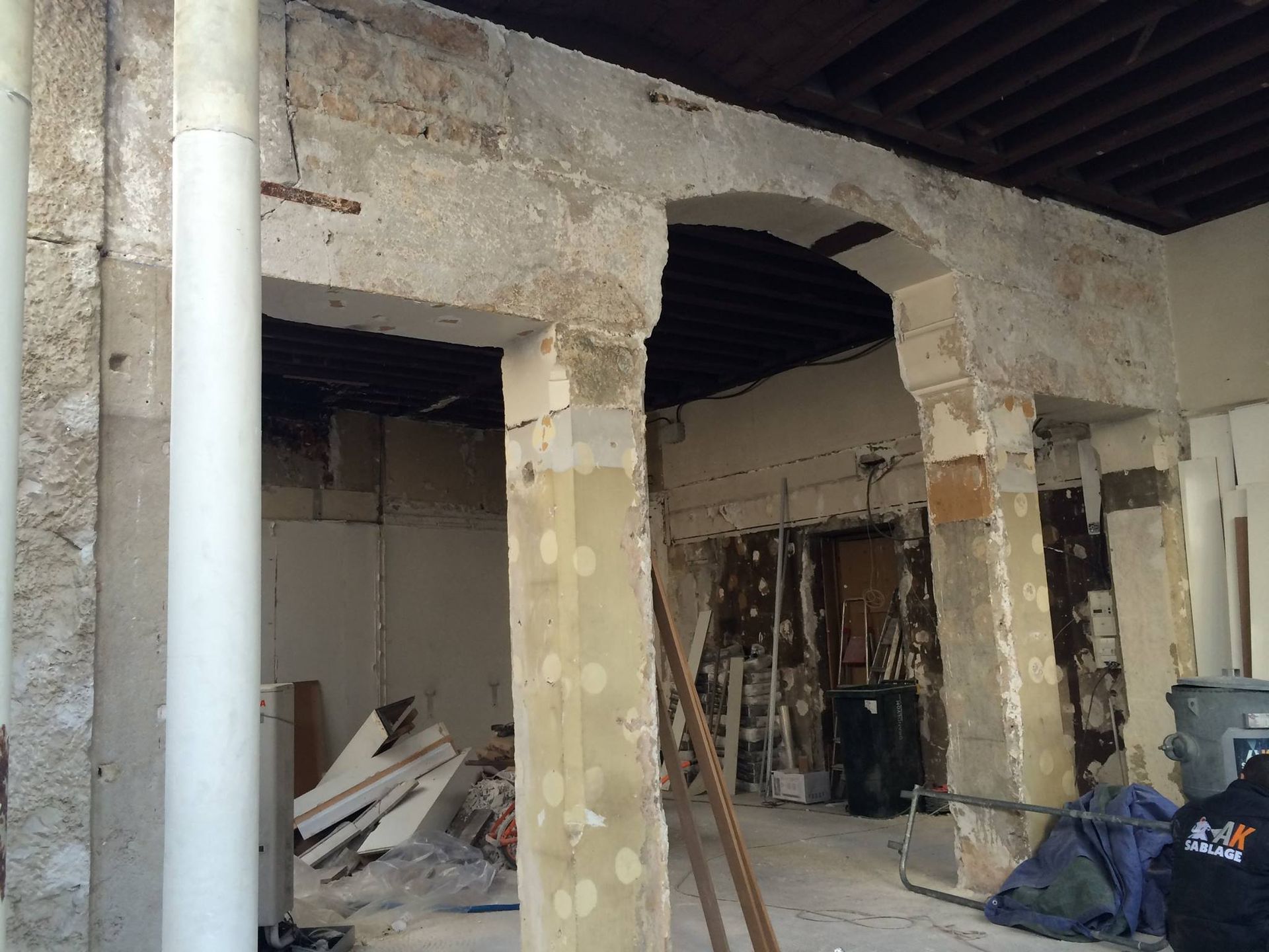 Intérieur d'un bâtiment en cours de rénovation, montrant des colonnes en pierre apparentes et une arche avec des débris.