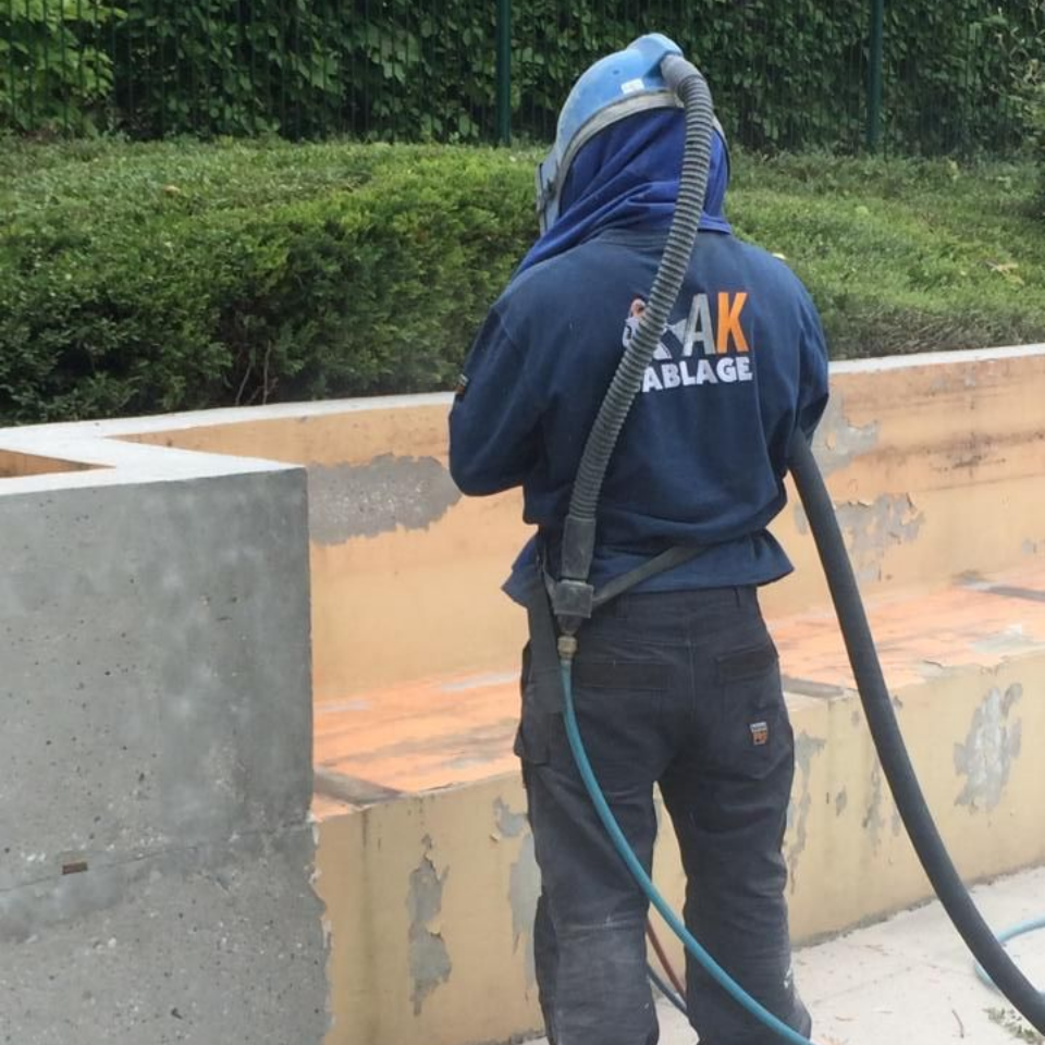 Une personne portant un équipement de sécurité sable une structure en béton à l'extérieur.