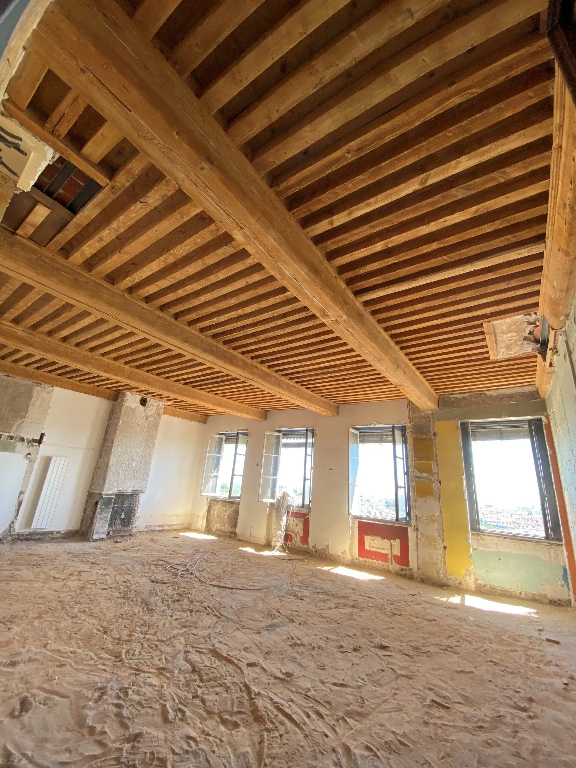 Vue intérieure d'une pièce en rénovation, présentant des poutres en bois.