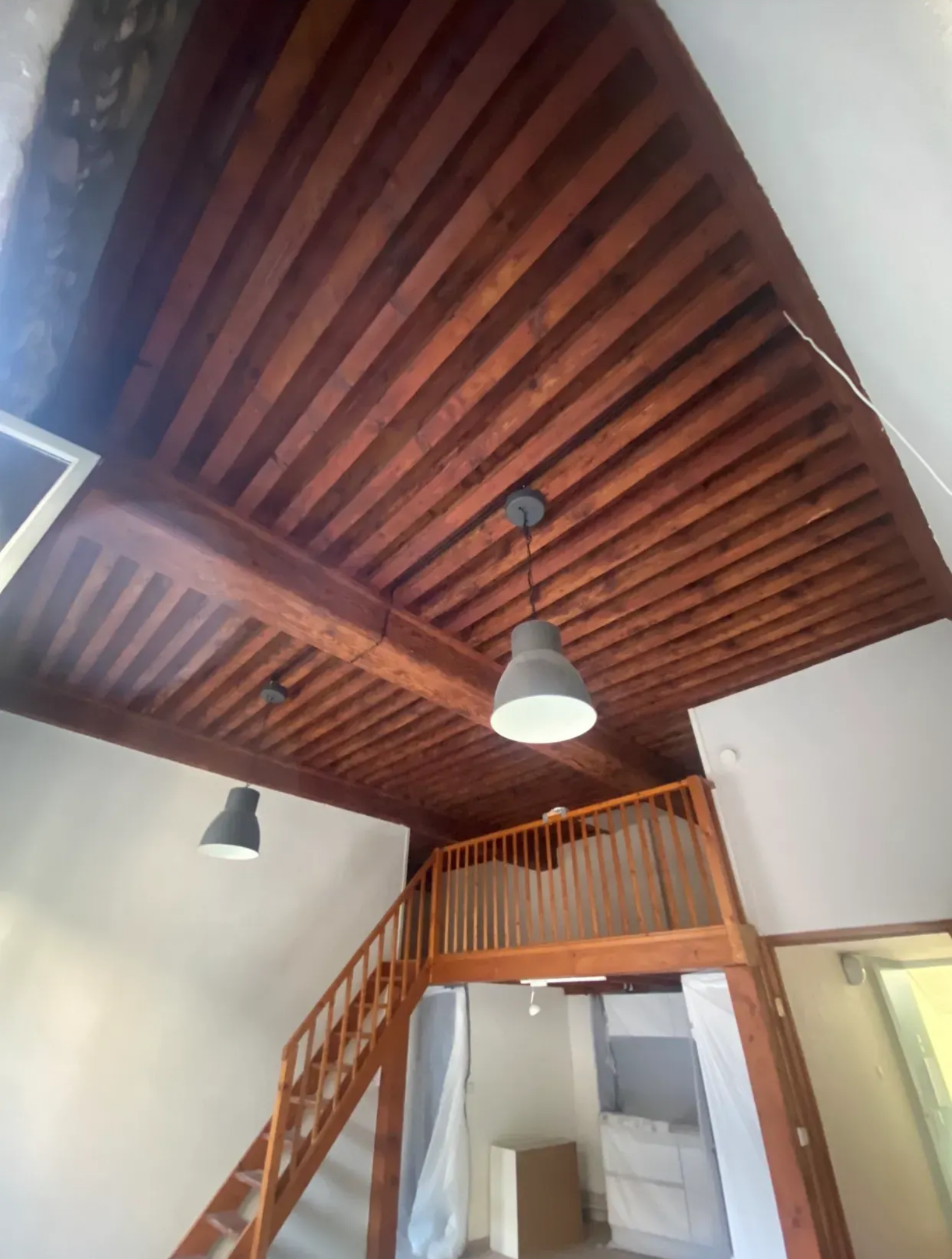 Plafond en bois avec poutres apparentes, escalier menant à une mezzanine et deux lampes suspendues.