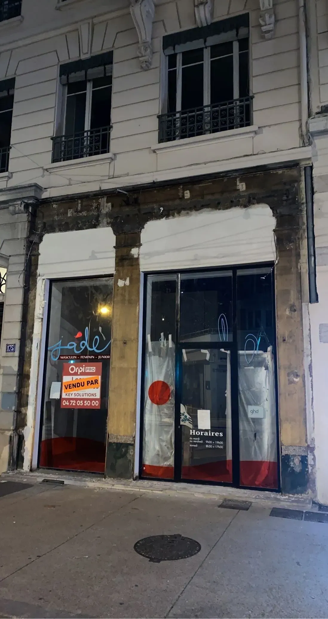 Vue extérieure d'un commerce fermé avec volets roulants. Apparence rouge sur la devanture, immeuble de deux étages.