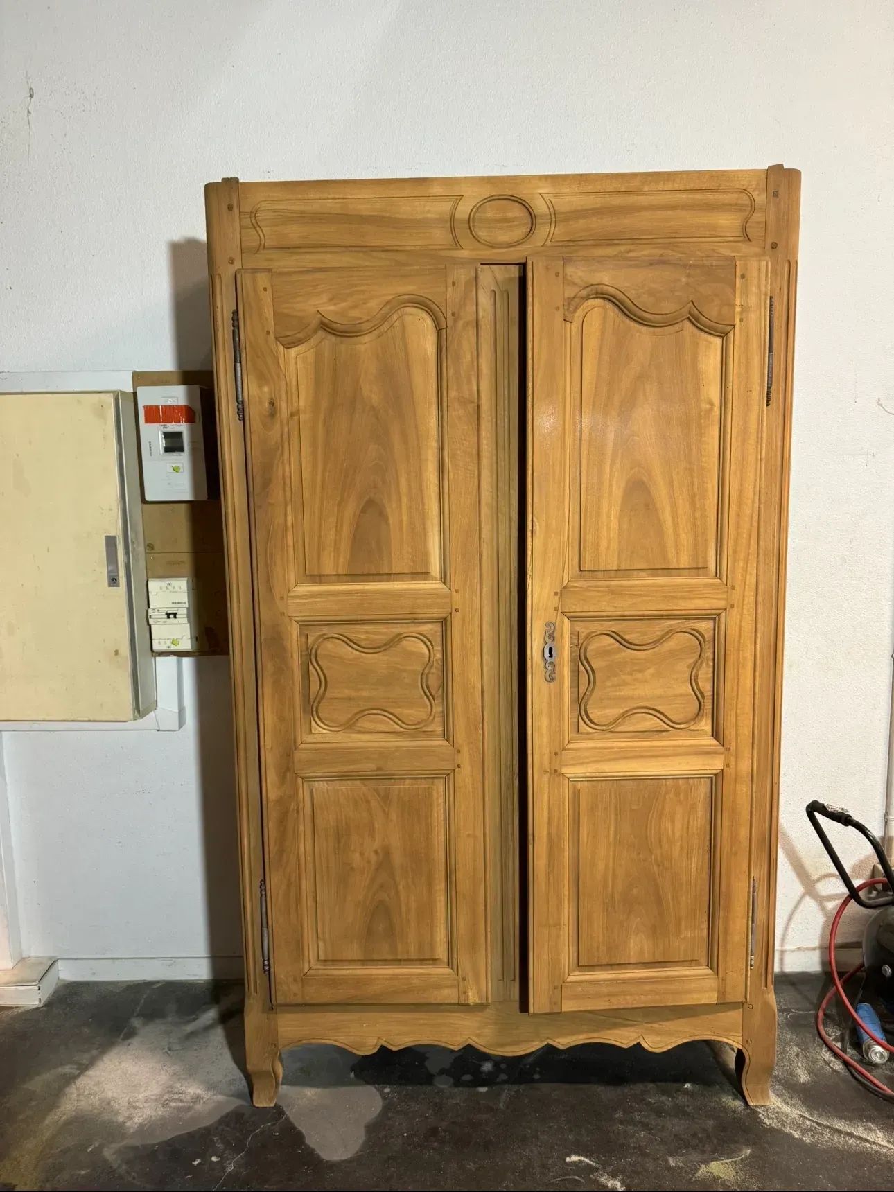 Armoire en bois à deux portes, détails sculptés, dans une pièce.