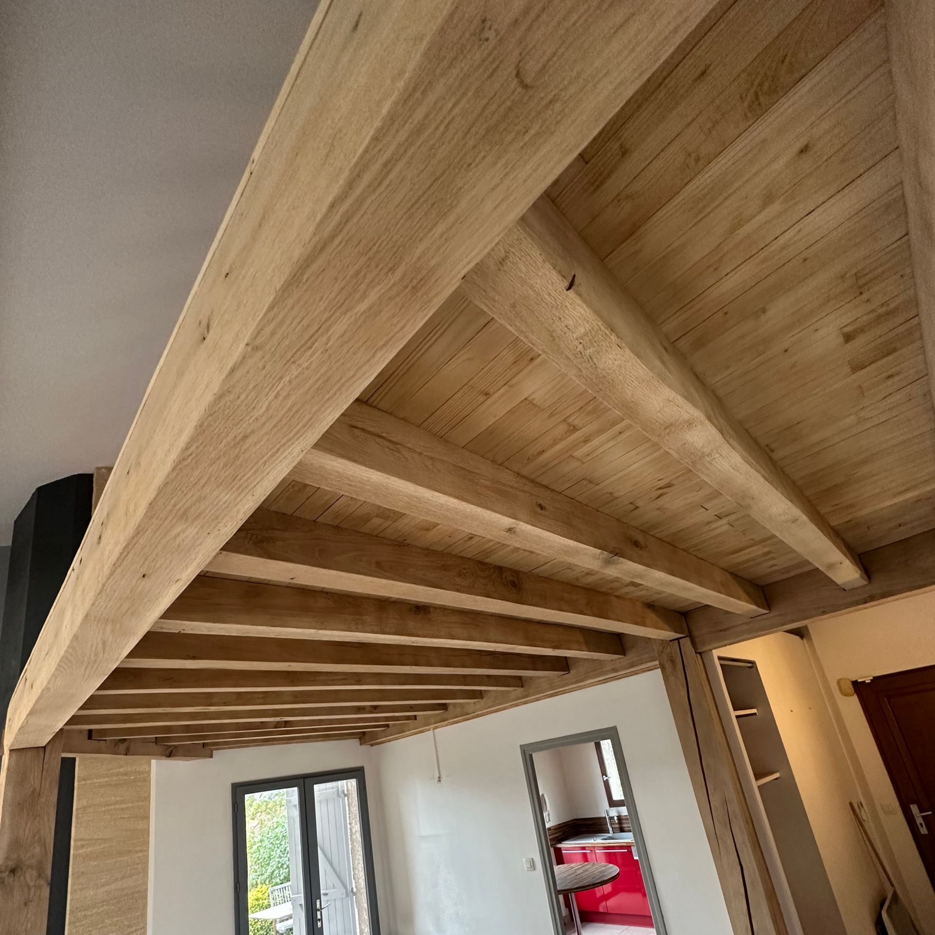 Plafond en bois avec poutres dans une pièce avec une fenêtre et des murs blancs.