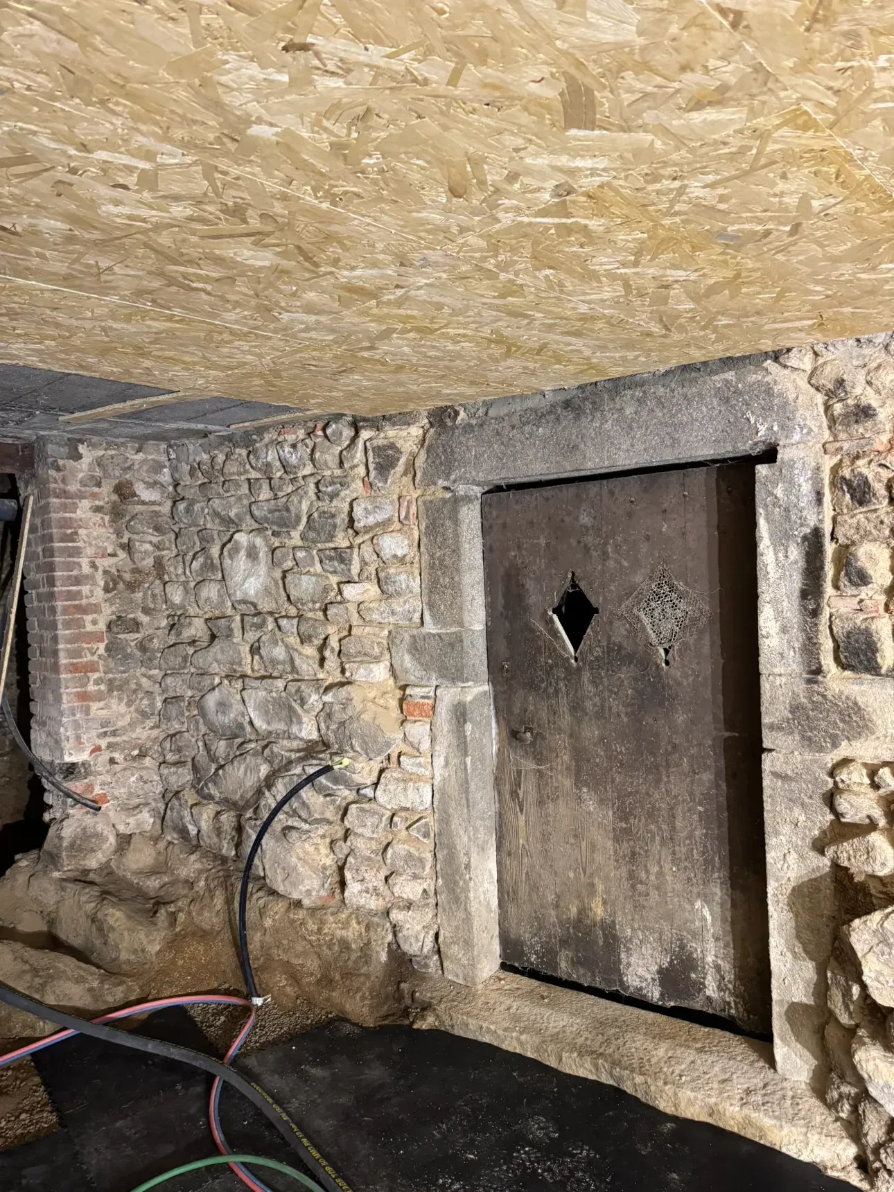 Mur de pierre et porte en bois patiné dans une cave.