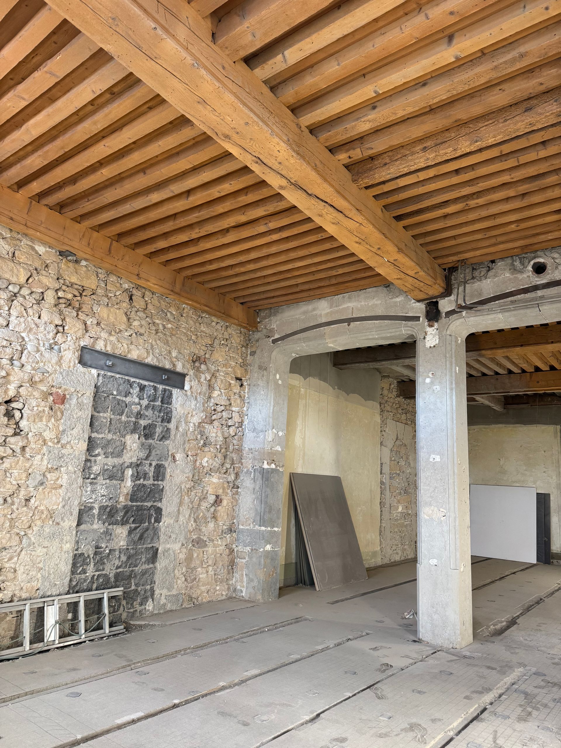 Intérieur d'un bâtiment aux murs de pierre, poutres en bois et pilier en béton.