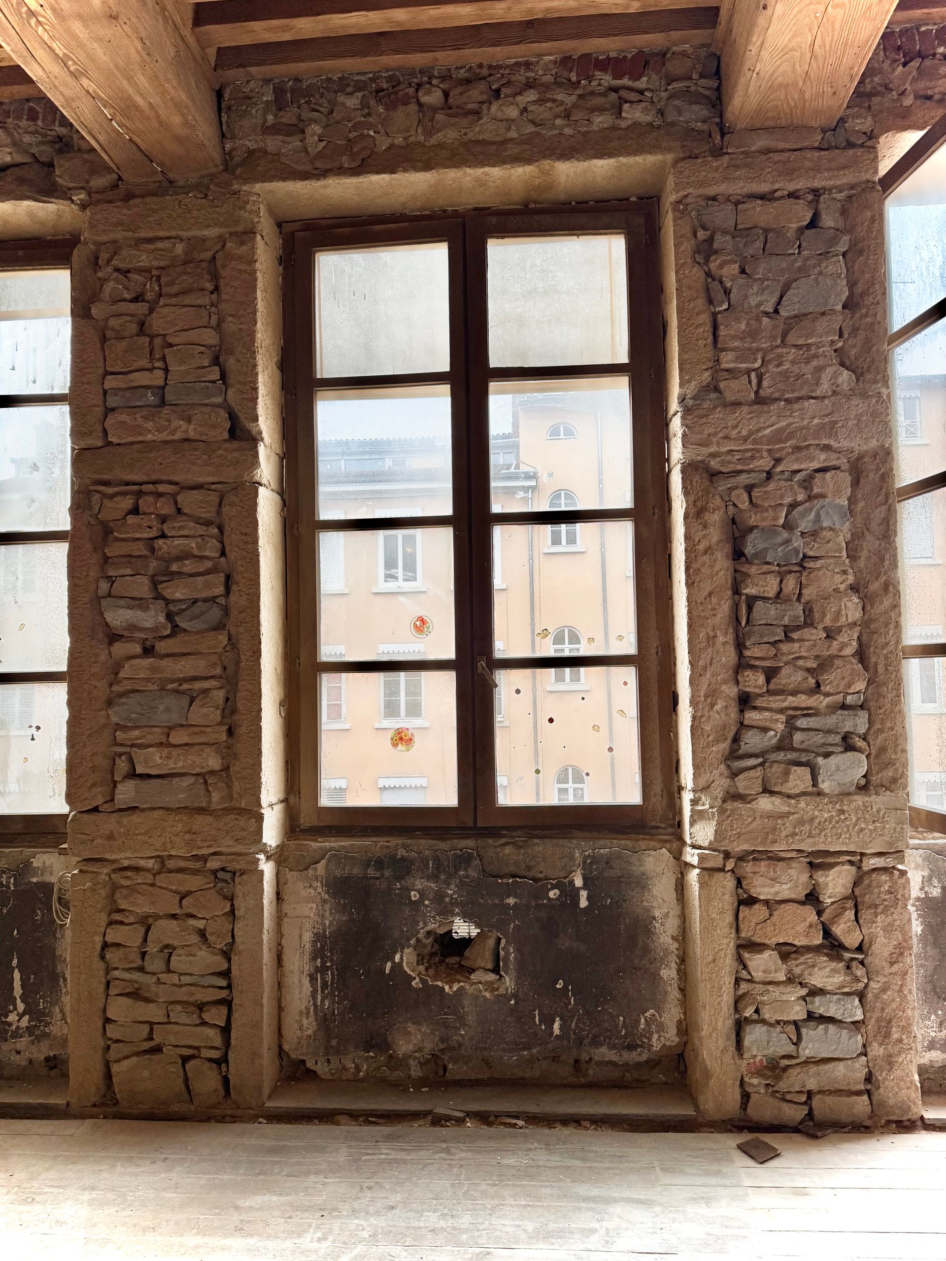 Fenêtre encadrée par un mur de pierre donnant sur un bâtiment