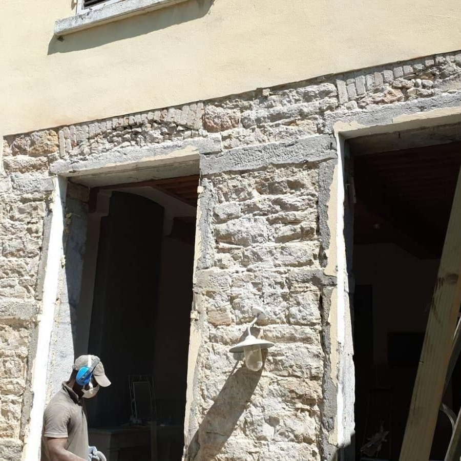 Homme travaillant sur la façade d'un bâtiment en pierre avec briques apparentes et portes.