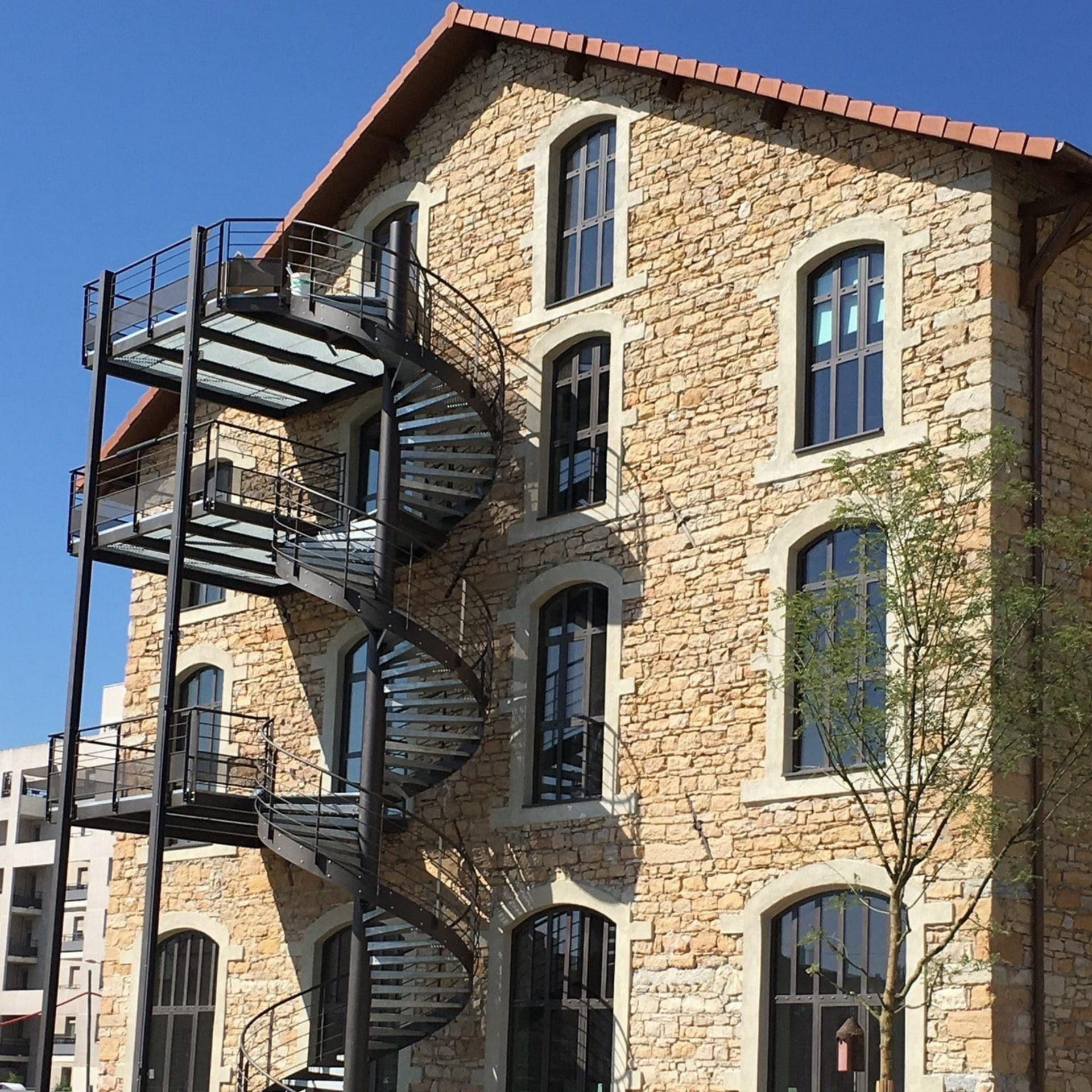 Bâtiment en pierre avec escalier extérieur en colimaçon contre un ciel bleu clair.