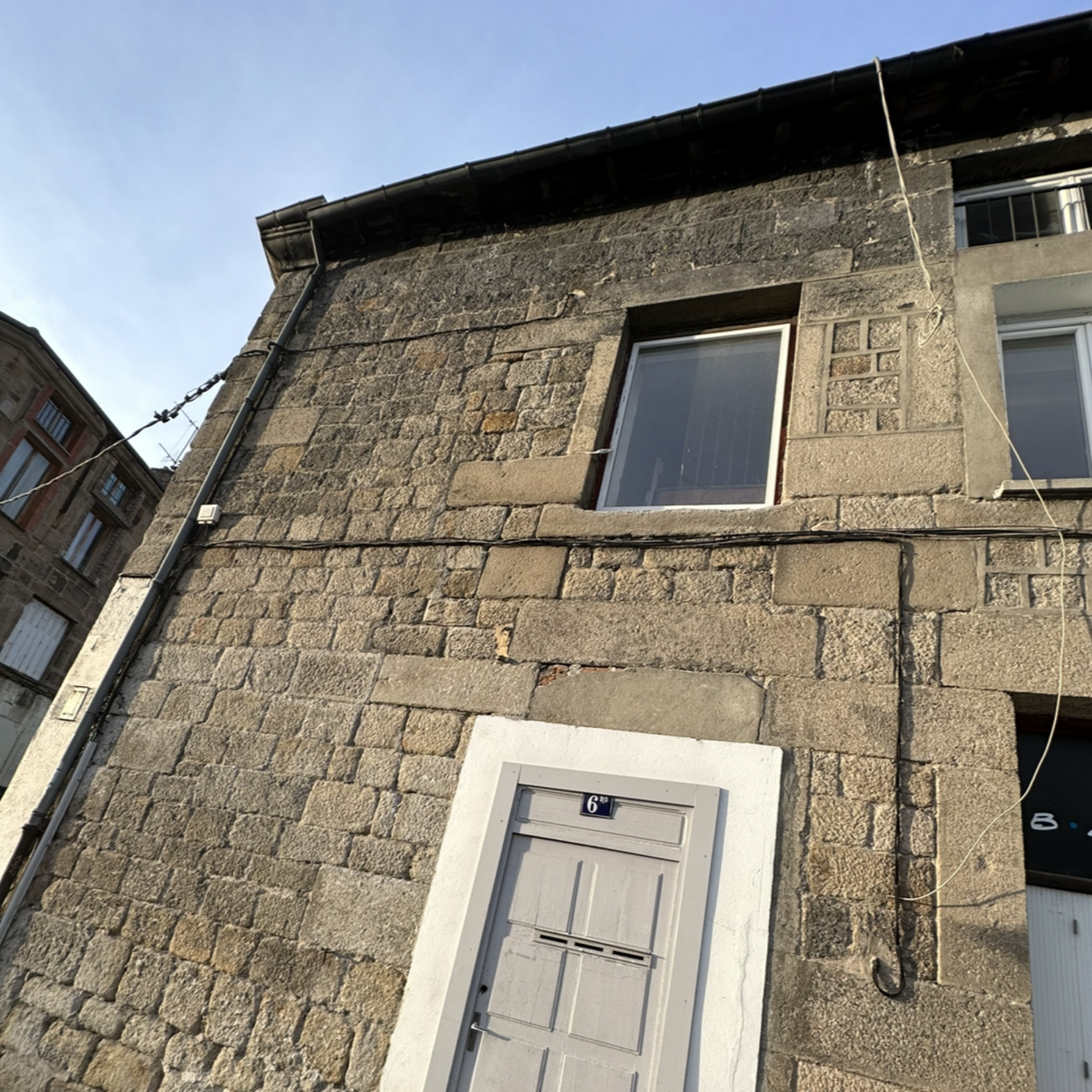 Façade d'un bâtiment en pierre avec porte et fenêtre grises.