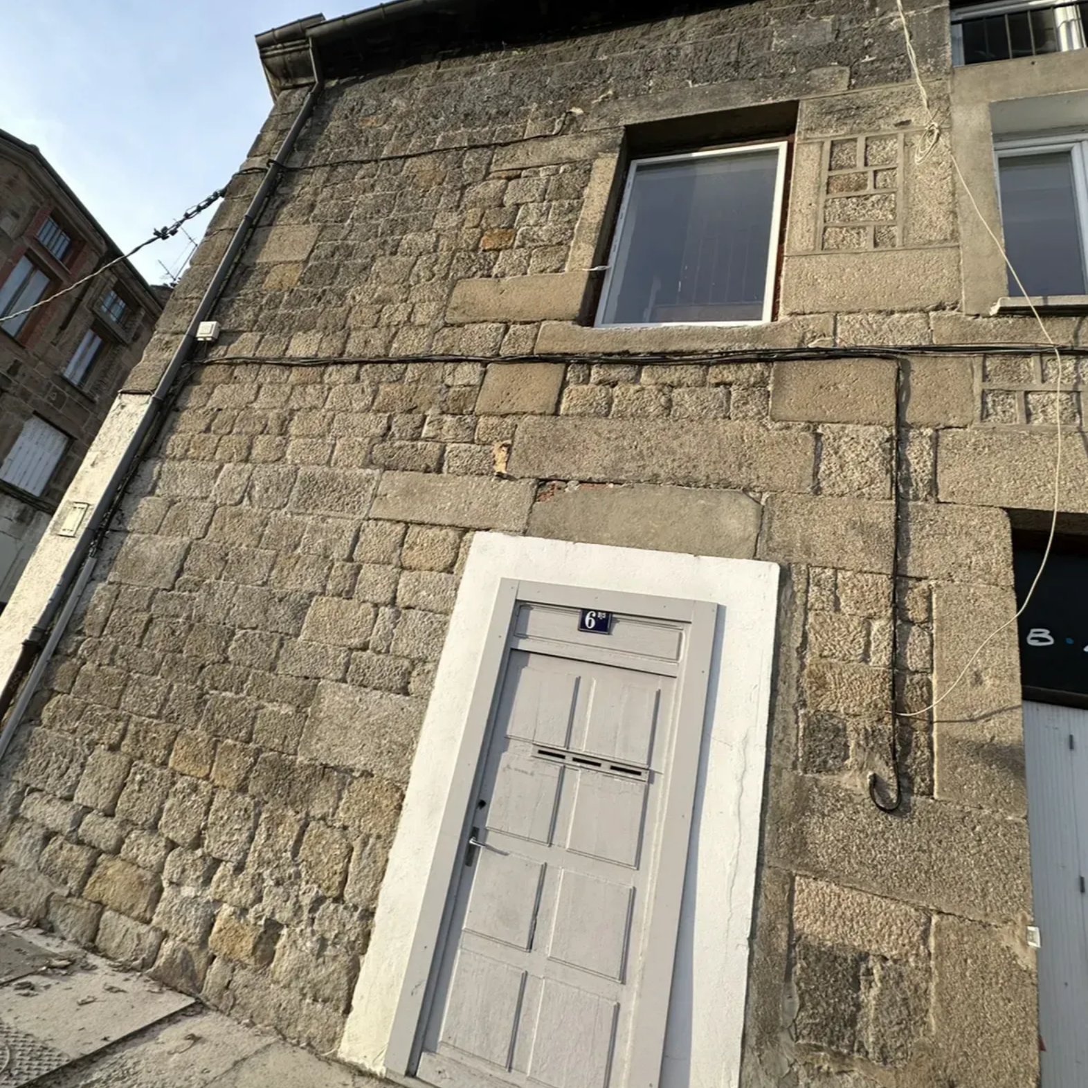 Bâtiment en pierre avec porte et fenêtre grises.