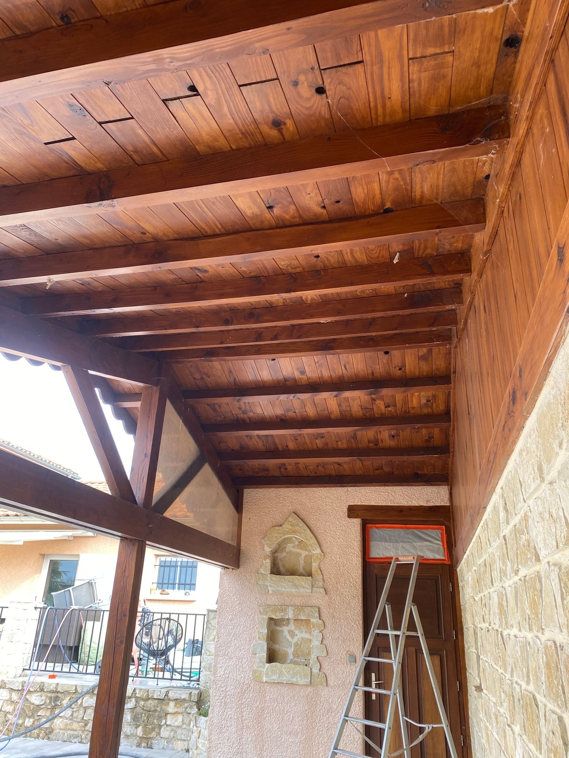 Plafond et poutres en bois au-dessus de l'entrée d'un bâtiment en pierre.