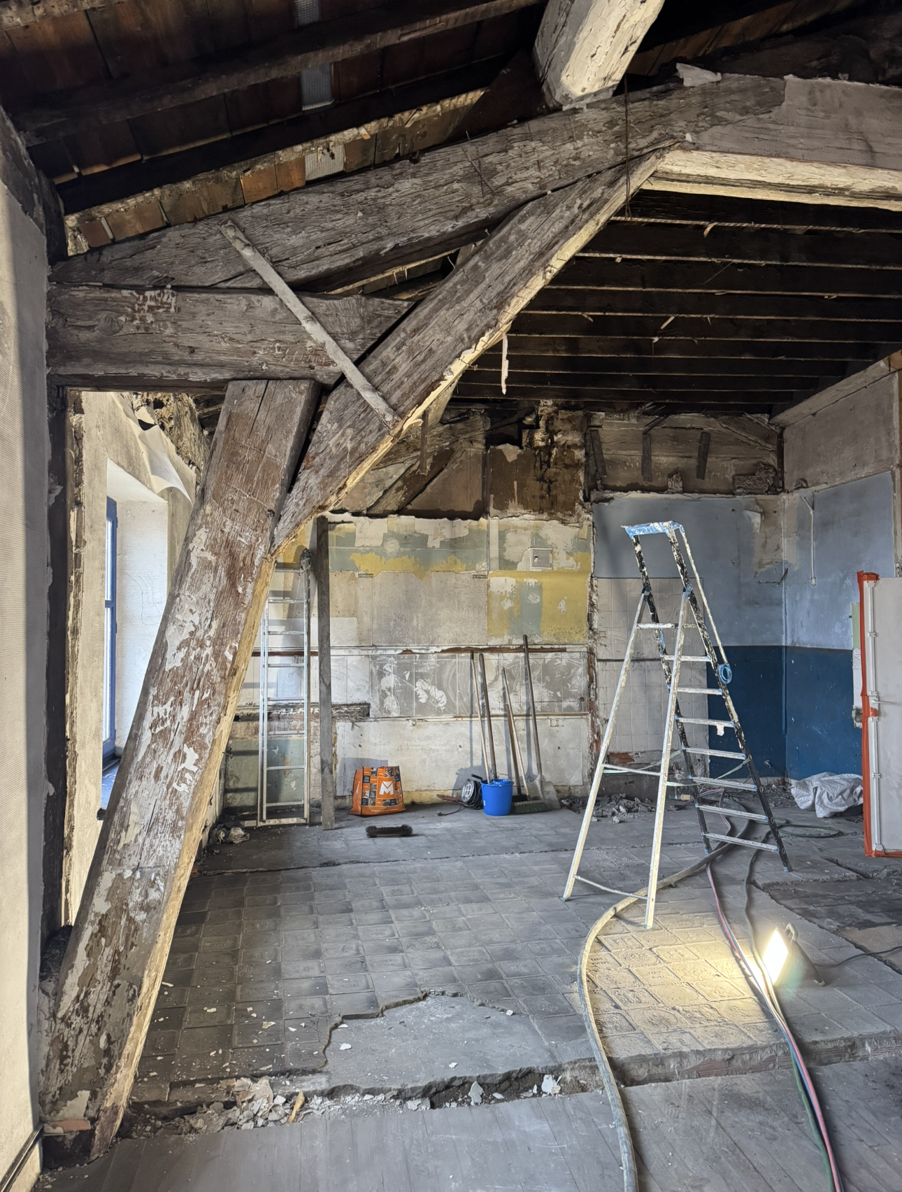 Poutres en bois apparentes, échelle, débris et murs nus.