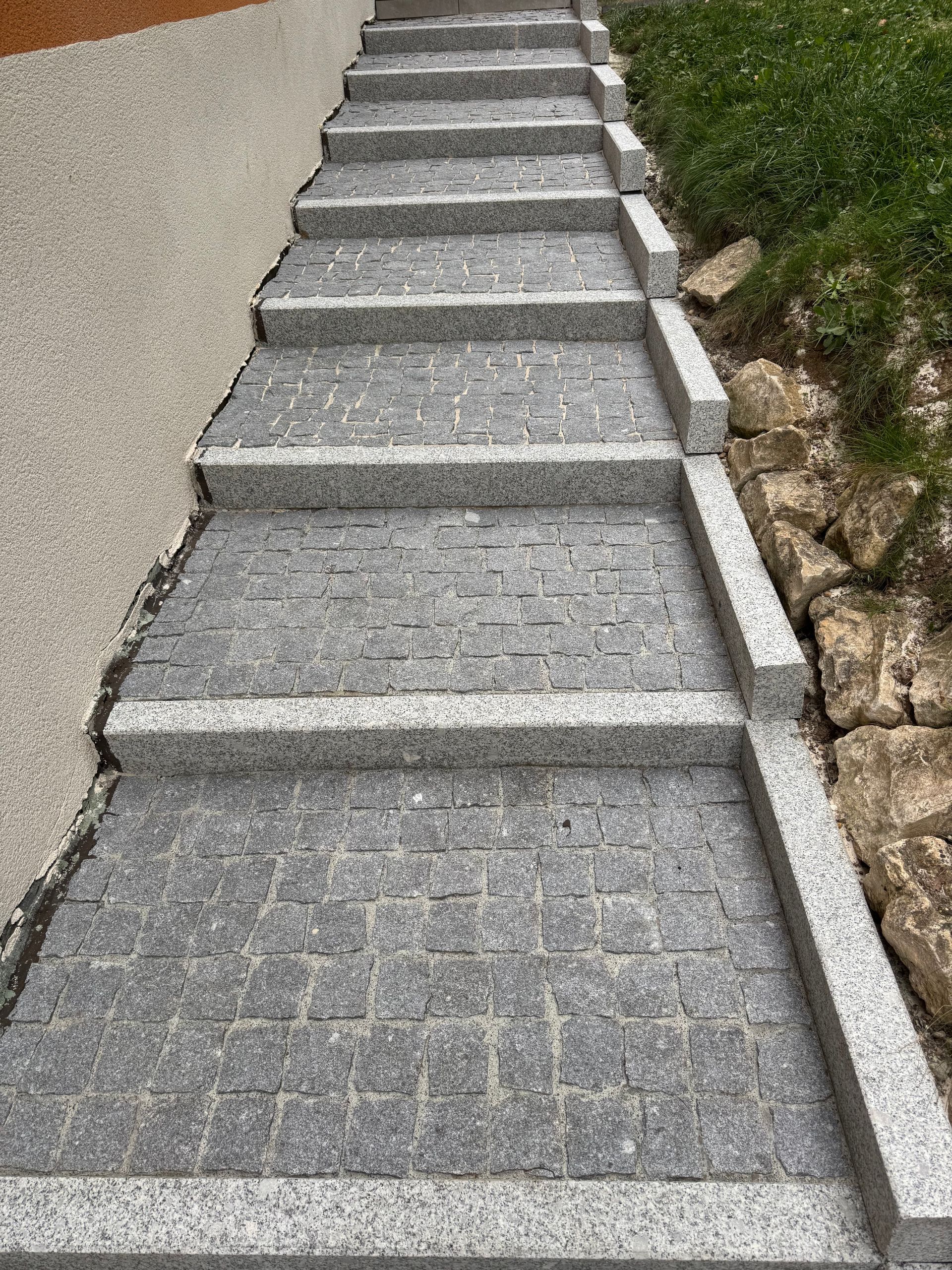 Escalier en pierre montant une colline, bordé de gravier et d'herbe.