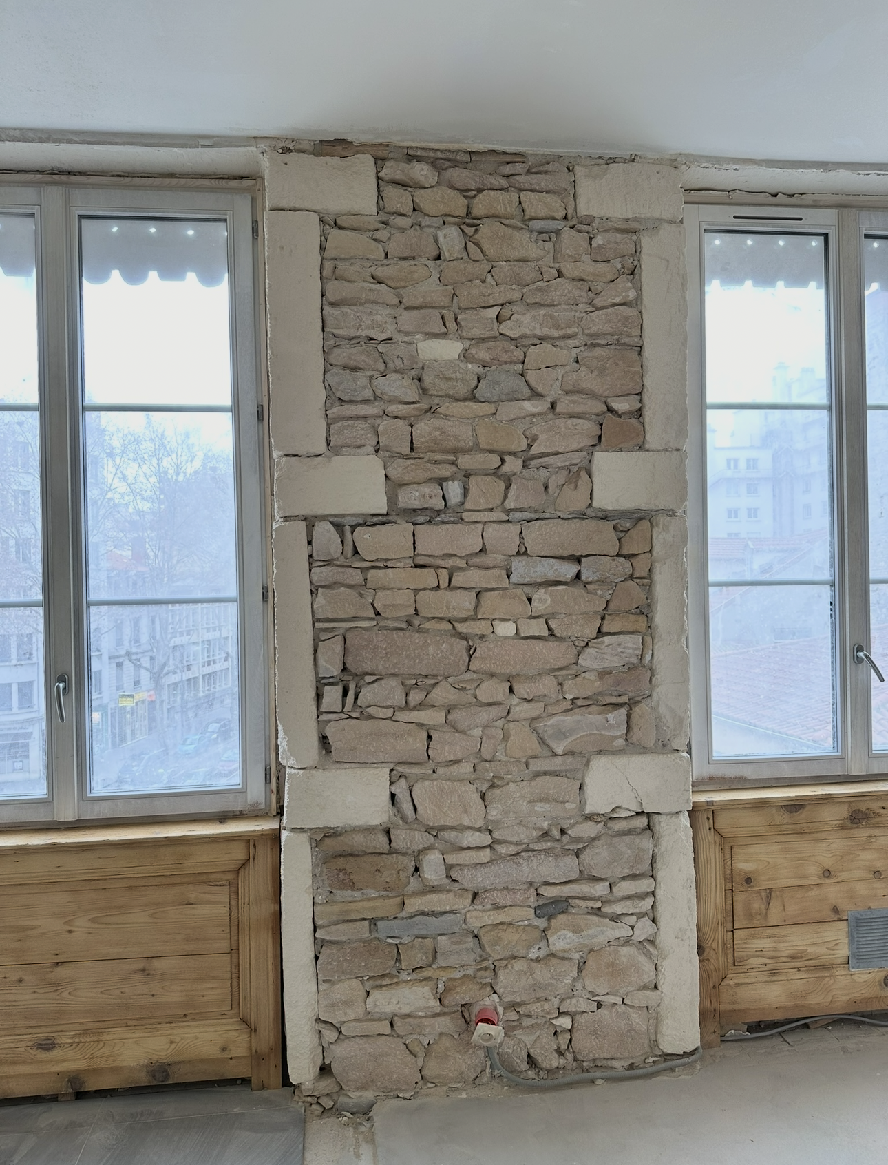 Section de mur en pierre encadrée de fenêtres, avec des blocs irréguliers de couleur claire et des bordures décoratives en pierre.