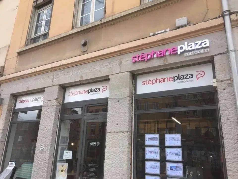 Une agence immobilière, Stephane Plaza Immobilier, avec une enseigne et des vitrines roses, dans une rue de la ville.