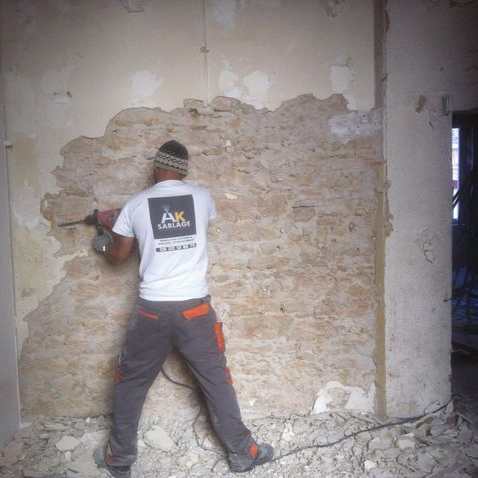 Un homme démolit un mur avec une perceuse dans un chantier de construction.