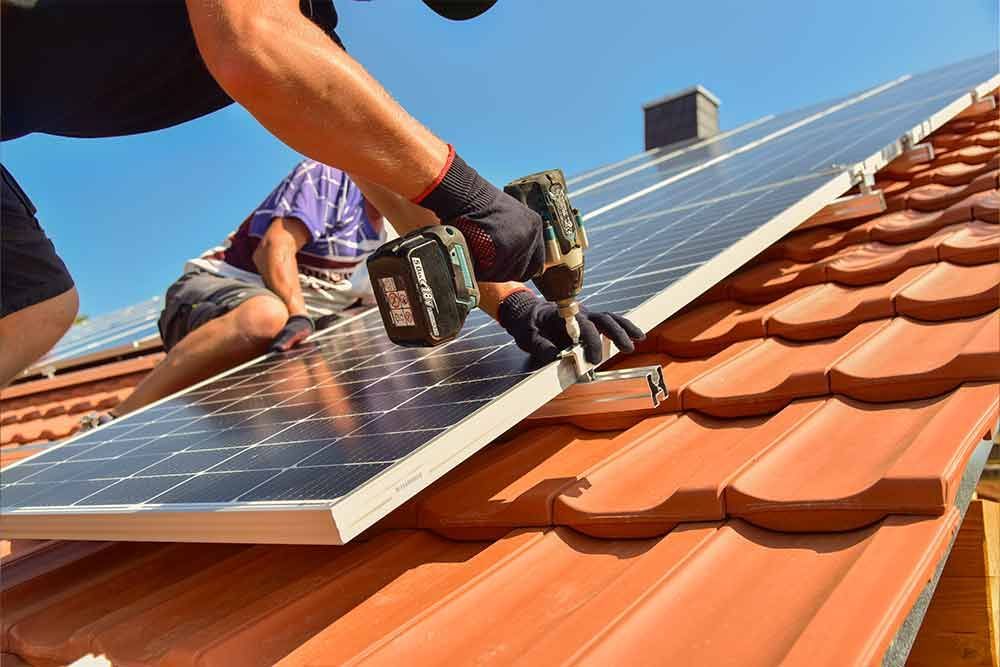 Ein Mann installiert Solarmodule auf dem Dach eines Hauses.