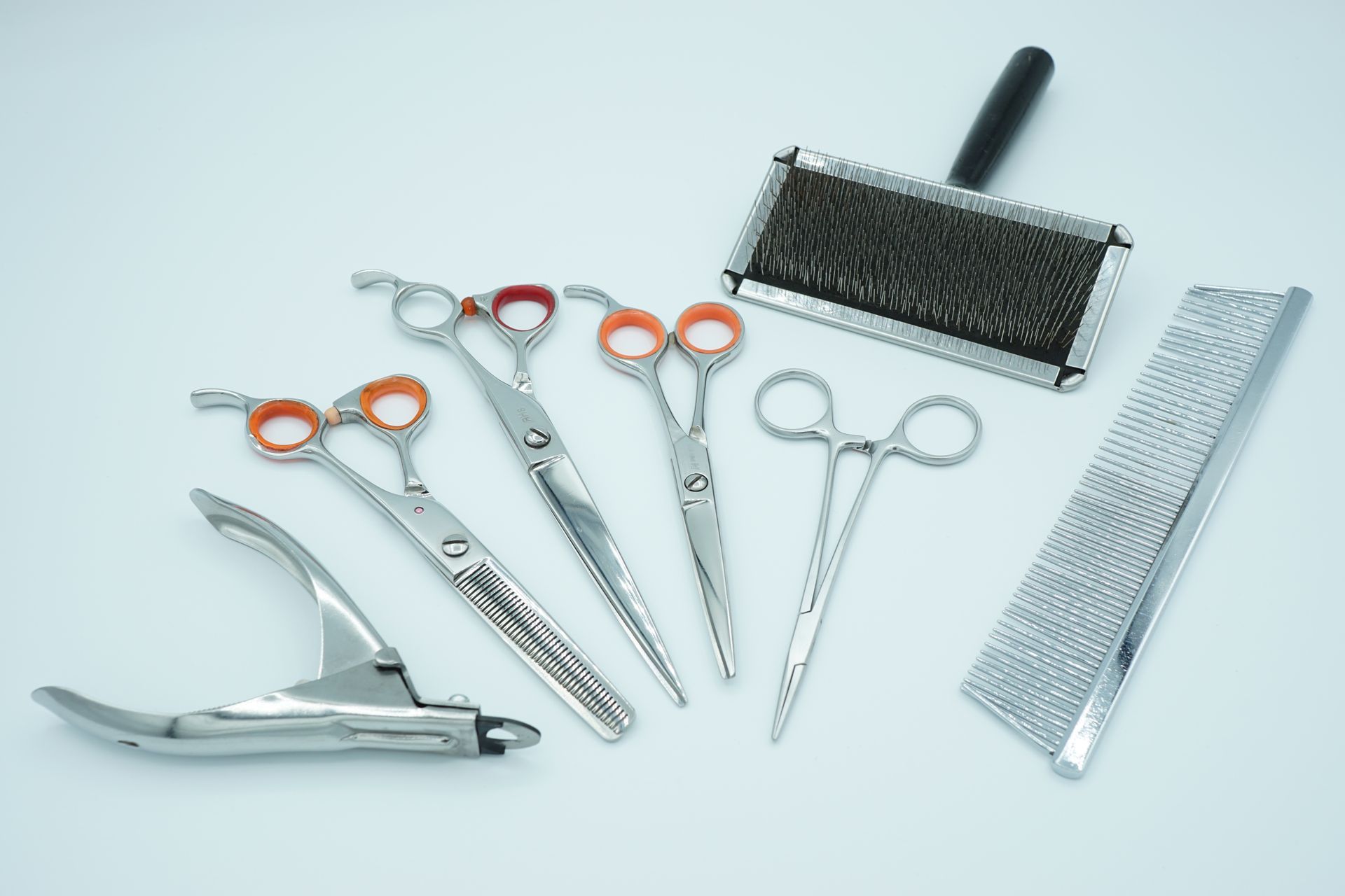 Outils de coiffure : ciseaux, ciseaux à effiler, peigne, brosse pour tondeuse et peigne métallique sur fond blanc
