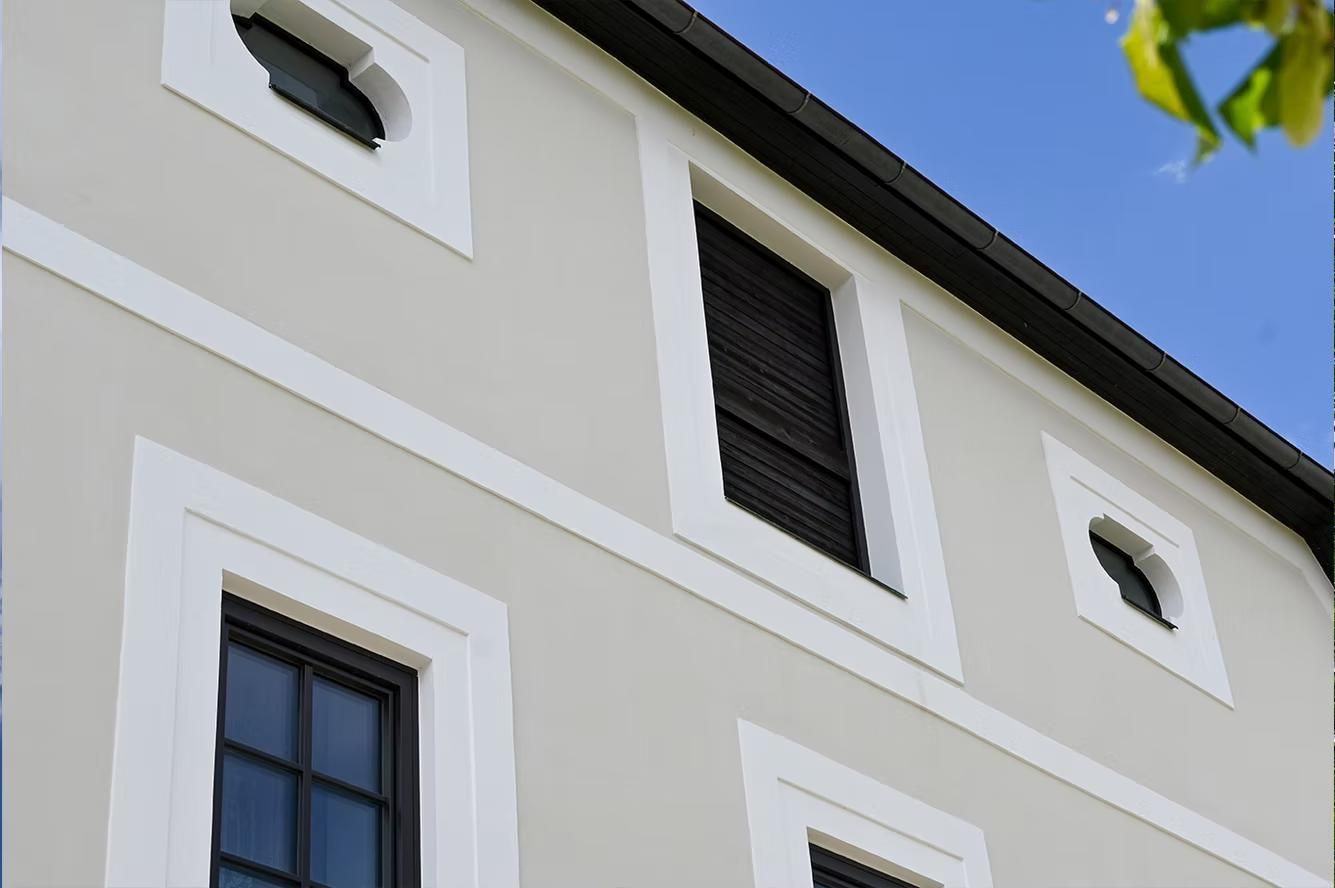 Ein weißes Gebäude mit schwarzen Fenstern und einem Baum im Hintergrund