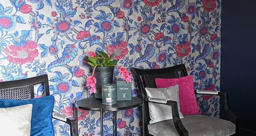 Ein Wohnzimmer mit zwei Stühlen, einem Tisch und einer geblümten Tapete.