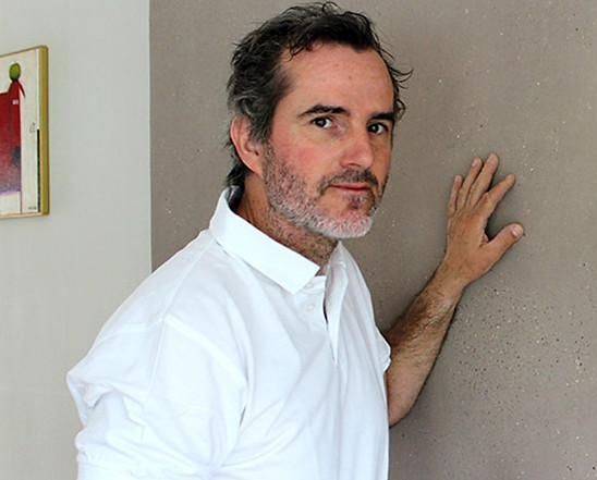 Ein Mann mit Bart lehnt mit seiner Hand an einer Wand.