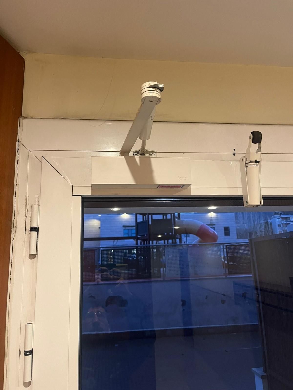 Puerta blanca con panel de vidrio y dos cierrapuertas superiores instalados en el interior.