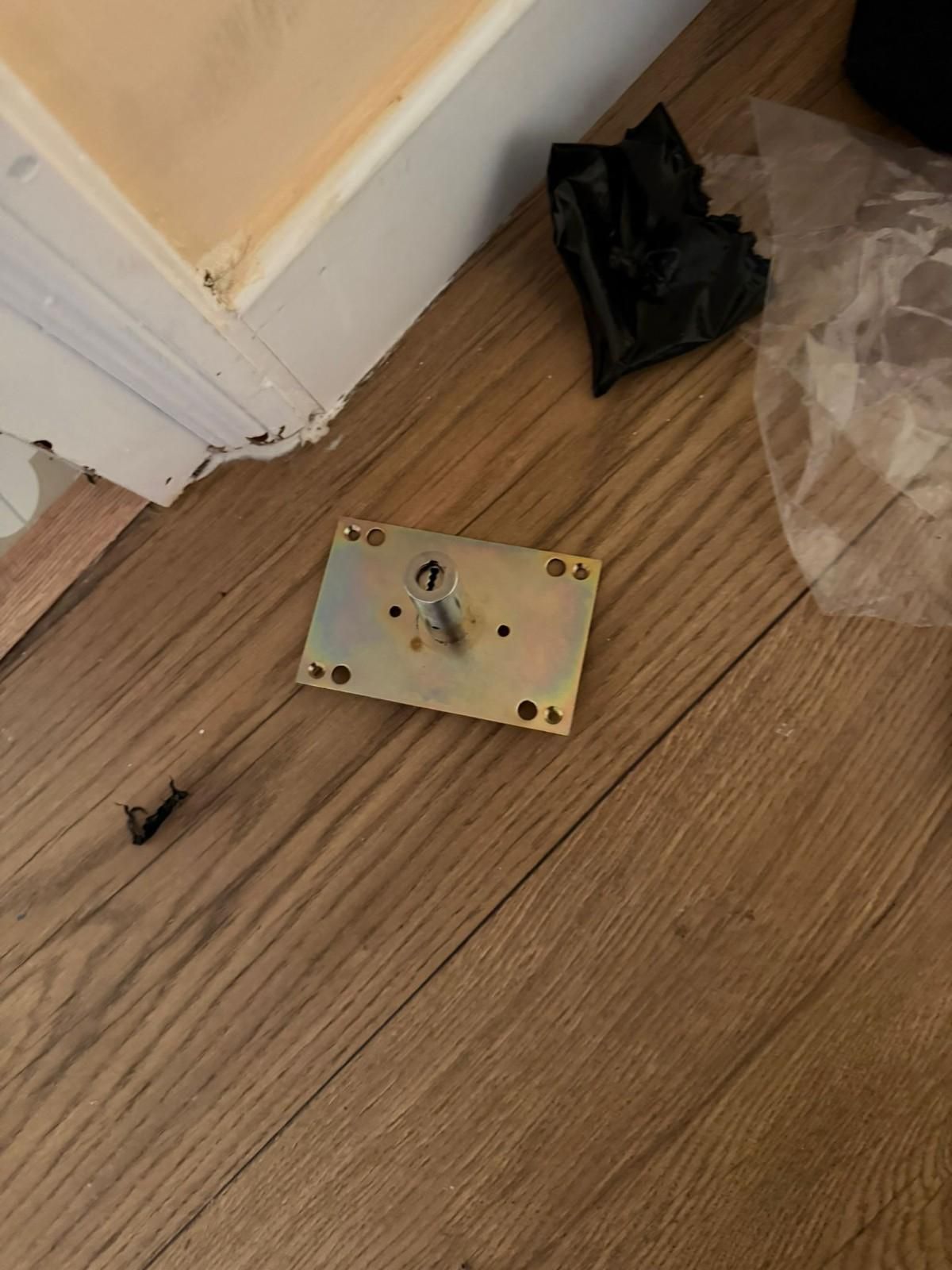 Suelo de madera cerca de una puerta con una pequeña pizarra blanca, una bolsa de plástico negra y un envoltorio de plástico transparente.