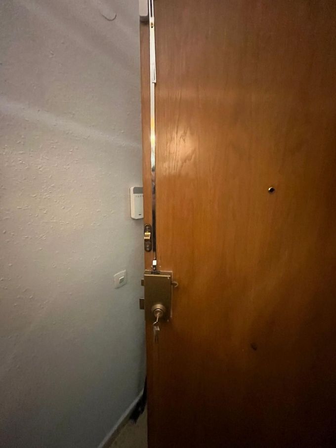 Estrecho espacio entre una puerta gris y una puerta de madera, que deja ver el pestillo de la puerta y el borde del pasillo.