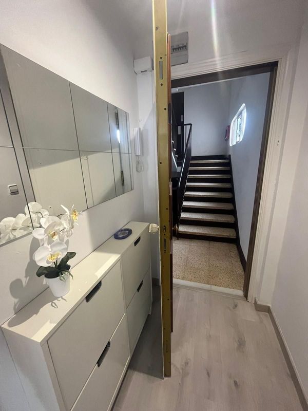 Pasillo luminoso con armarios de almacenamiento, orquídeas y una escalera que conduce a la planta superior.