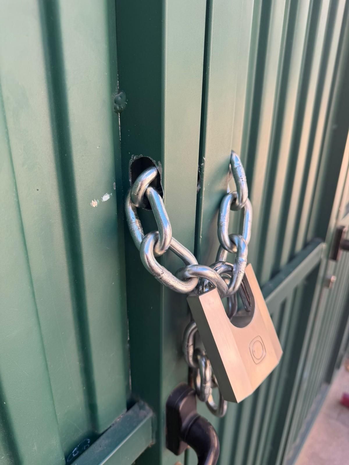 Candado y cadena que aseguran una puerta metálica verde