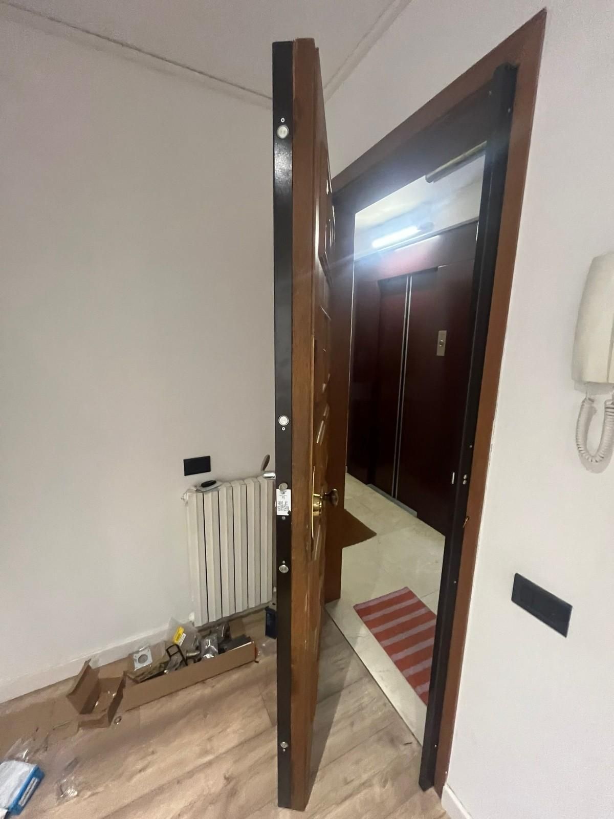 Puerta del apartamento abierta con vista al pasillo, radiador y pequeños objetos en el suelo del interior.